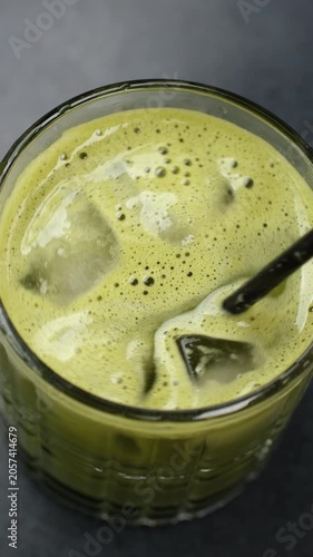 Hand stirring Refreshing matcha tea with black straw, close up