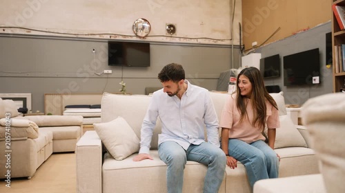Young couple choosing and testing a sofa in a furniture store showroom
