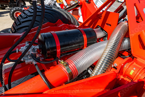 Tight detail of bright red painted metal machinery showing braided stainless hoses, hydraulic cylinder, rubber hoses, fittings and mounting brackets