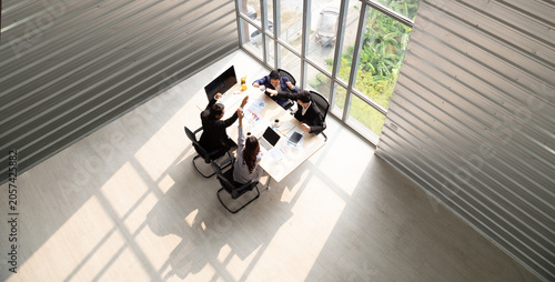 Aerial top view of diverse business team having a meeting around a conference table with laptops and documents in a bright modern office with large windows