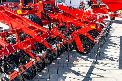 Quadro su tela Bright red multi-row seed drill machinery arranged in a row on a concrete yard under strong daylight