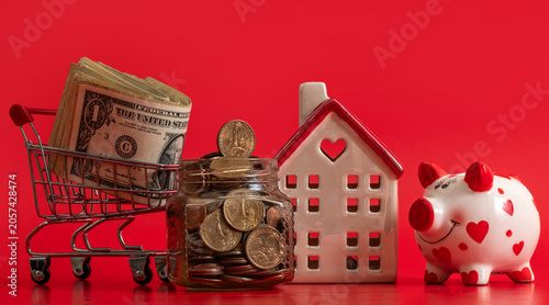 Canvas Print A glass jar with US coins, a symbolic house, US $1 bills and a piggy bank on a r