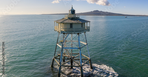 Auckland's Rangitoto Island is visible in the distance from the historic Bean Rock Lighthouse in Waitemata Harbour, New Zealand. The lighthouse guides ships.
