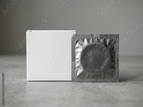 A discreet sterile foil-wrapped prophylactic and its accompanying blank cardboard packaging rest side-by-side on a textured grey surface, promoting responsible reproductive choices