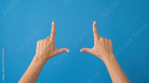 Woman hands making rectangle frame gesture with fingers on blue background