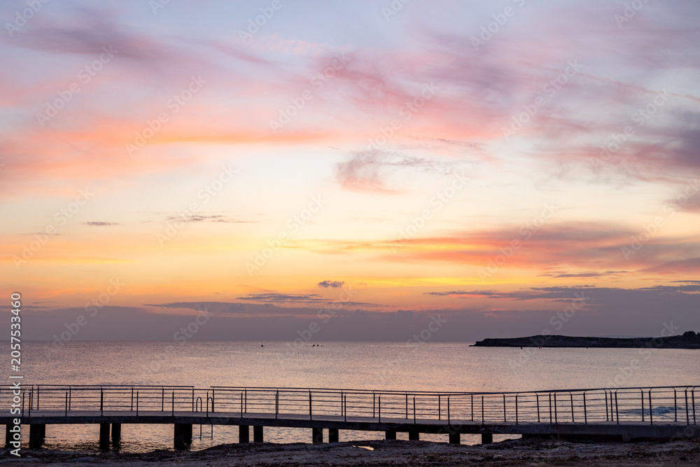 Fototapeta premium Peaceful and calm mediterranean sea under beautiful pastel pink sunset sky in winter low season. Quiet twilight marine landscape with pedestrian walking promenade walkway, Ayia Napa, Cyprus