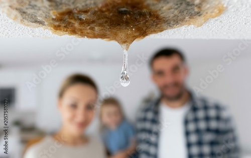 Water Droplet Falling from Damaged Ceiling Inside Residential Home with Family in Background