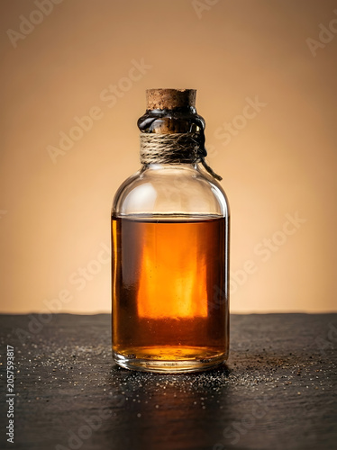 Transparent glass bottle with cork lid and liquid on dark surface