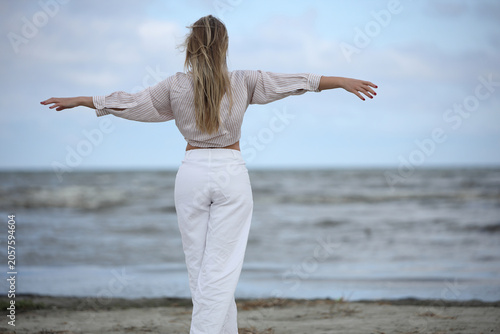 Woman standing on beach with arms outstretched facing sea