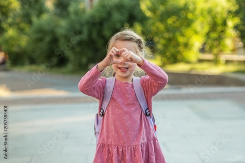 Happy child with backpack making heart shape with hands before school