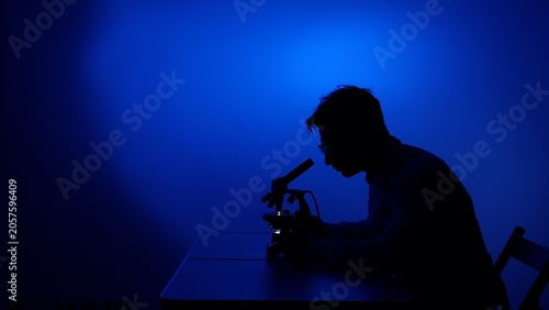 Obraz na plátně Scientist silhouette closely observing samples under a microscope, conducting sc