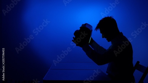 Photography Silhouette of a person at a desk holding a vr headset, immersed in blue lit digi