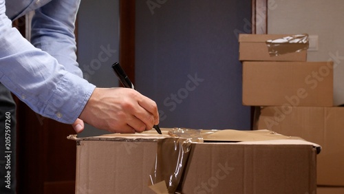 Cuadro en lienzo Person's hand writing recipient address and shipping details on taped cardboard
