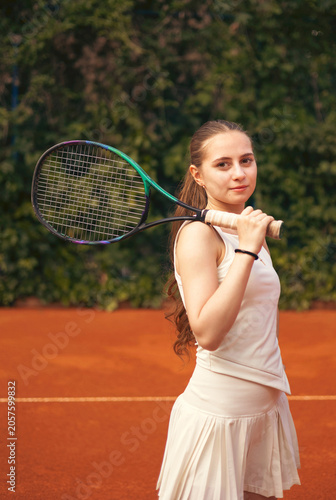 Young female tennis player standing on a tennis court holding a racket, natural daylight, athletic and focused expression, dynamic sports atmosphere
