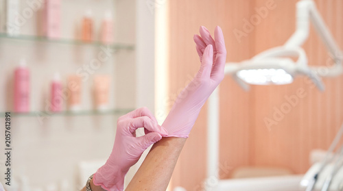 Medical professional putting on long pink nitrile glove on hand in aesthetic clinic close up