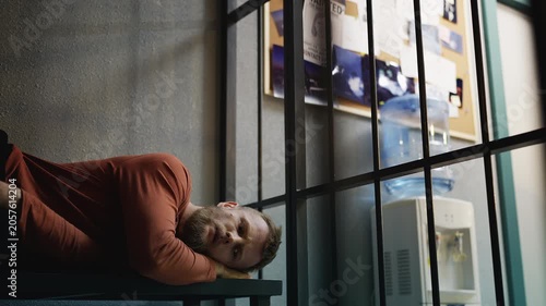 Nervous male detainee lying on a bench inside a jail cell, awaiting trial