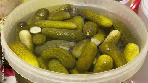 Fresh market pickles in container, closeup of clear plastic tub packed with brined cucumbers, glistening brine