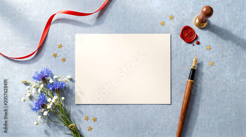 A bouquet of flowers, a pen, and a blank card on a blue fabric background with a red ribbon and gold stars