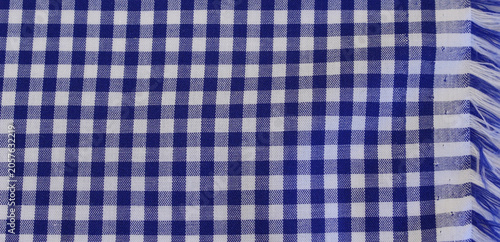 Texture of classic blue plaid cotton cloth with fringed edge. Close up of blue and white gingham fabric background. 