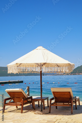 Beach vacation. Chaise lounges and beach umbrella on coast of  Bay of Kotor on sunny day. Montenegro. Copy space