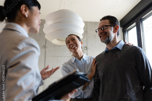 Happy diverse couple viewing a modern apartment with a professional real estate agent. Smiling multicultural clients discussing property buying, renting, or investing during a house tour.