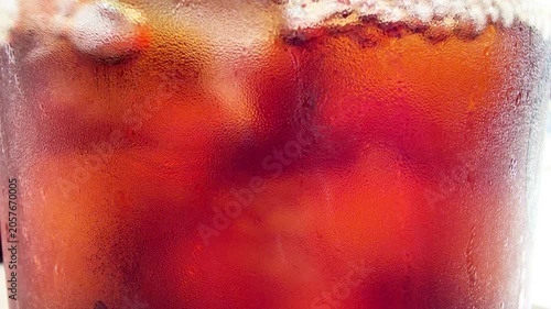 アイスコーヒーのクローズアップ。水滴がついたグラス。氷とコーヒーが回転する動画。