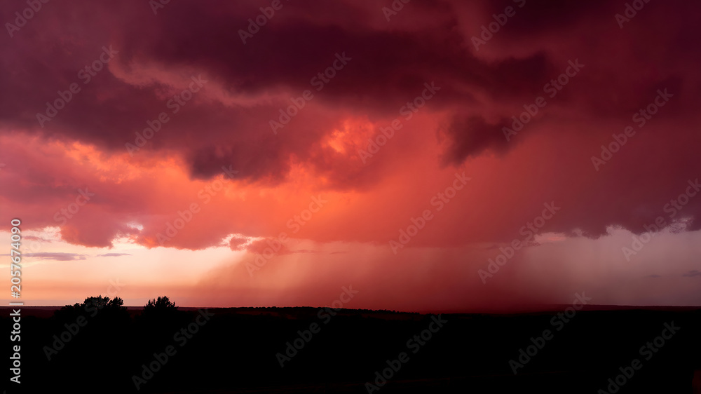 Obraz premium Spectacular Crimson Thundercloud Formation Illuminated by Sunset Above a Dark Countryside Horizon