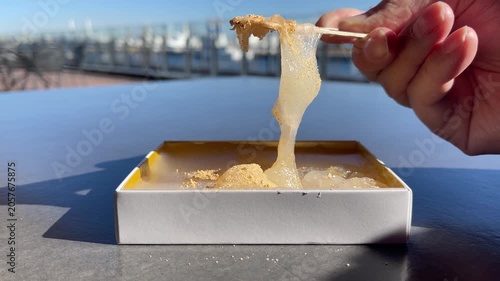 きな粉をトッピングした和菓子のわらび餅。食べたいけど切れず、力強く伸びているわらび餅の動画。