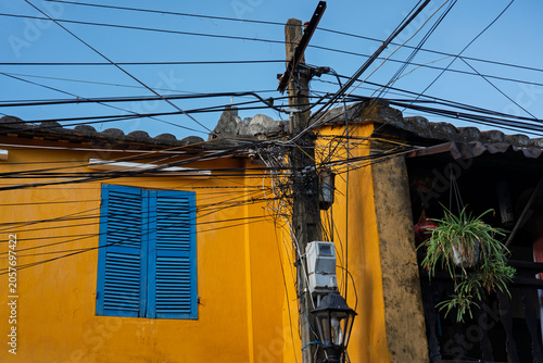 Overhead utility wires cross a yellow heritage building facade in Hoi An Ancient Town.
