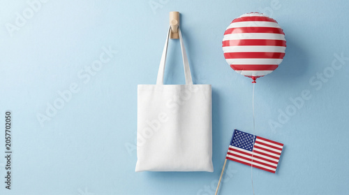 Blank white tote bag mockup hanging on blue wall with patriotic american flag balloon