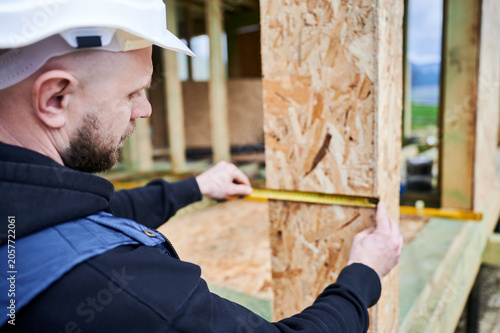 Construction professional checking dimensions of window or door opening in wooden panel, inspecting placement and build precision