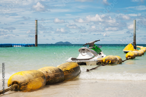 Jet skis parked by the shore on a clear day near the ocean with clouds and distant mountains in the background. Concept of sea vacation and tourism.