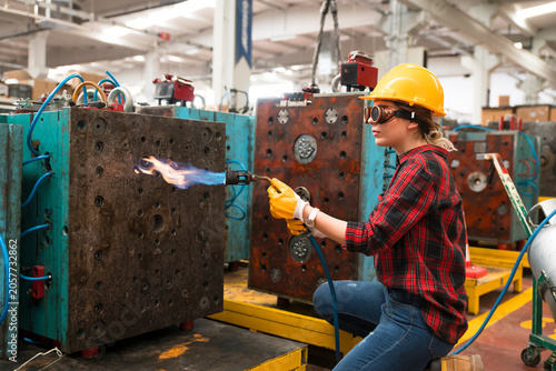 Foto Woman in hard hat using blowtorch on industrial mold in factory