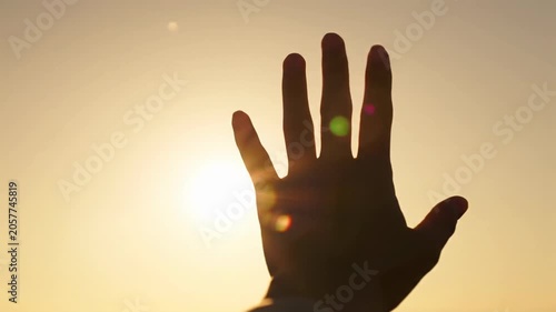 Clean human hand gently rises into an intensely backlit golden hour sky, sunbeams creating warm lens flares and ethereal light shafts through fingers, shallow depth of field with dreamy bokeh.