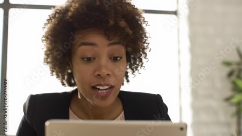 A professional woman, mid-30s, curly hair, tailored blazer, focuses on a tablet, experiencing a eureka moment in a sunlit office, dolly in to a close-up, shallow depth of field. Concept of