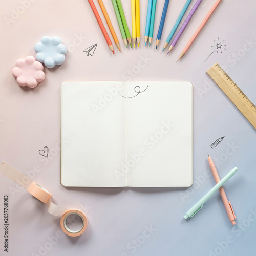Blank notebook lies centered among assorted colorful pencils and craft supplies on a smooth gradient backdrop.