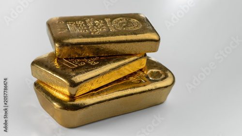 Three cast gold bars of different weight are in a pile, isolated on a white background.