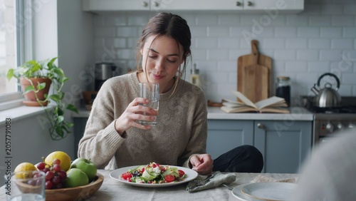 Woman eating healthy salad at modern kitchen table with fresh vegetables and fruits