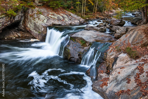 Baby Falls, Flowing water creates ripples near rocks in a forest during autumn in a river setting
