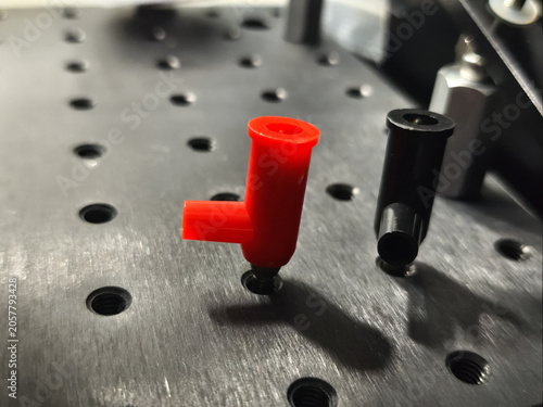 Laboratory fixture with red and black probe tip on metal plate, close up of precision testing setup