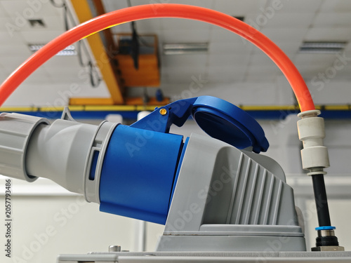 Industrial electric socket with red cable and blue cap on gray machinery in factory interior
