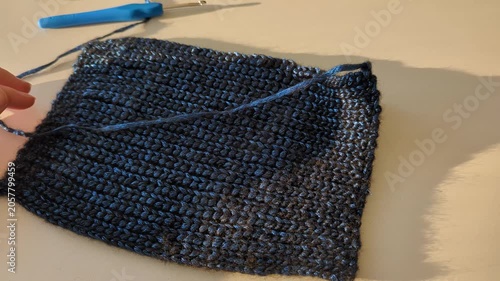 Hand with blue crochet hook making textured fabric, detailed craftsmanship