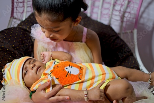 Sister holds baby brother dressed in cute outfit on a sofa