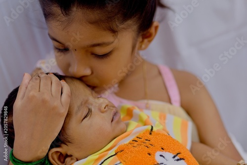 Sister kisses baby brother while sitting indoors