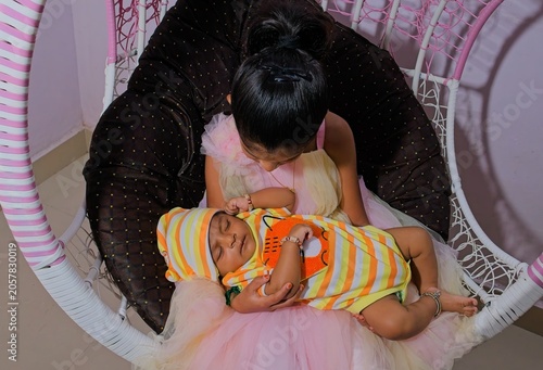 Sister sits in hanging chair with sleeping baby in colorful outfit