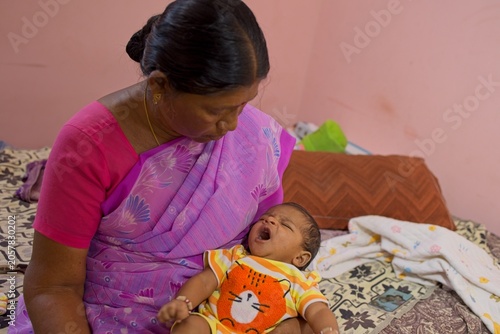 Woman holds baby while sitting on bed at home