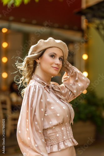 Portrait of a young blonde woman in a vintage pastel-colored outfit and a beret in the city center. Retro style.