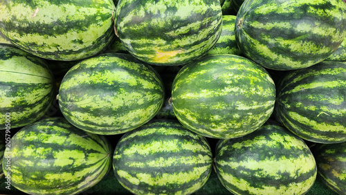A close-up view of a large pile of fresh whole striped watermelons on display at a market stall.