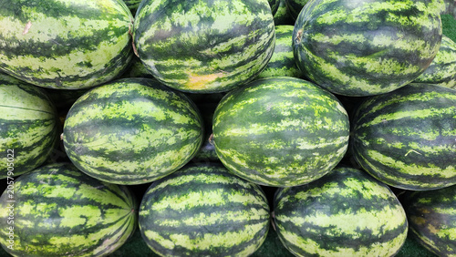 A close-up view of a large pile of fresh whole striped watermelons on display at a market stall.