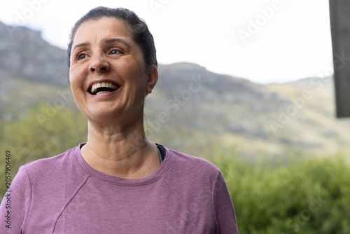Photos Mature woman laughing, standing on porch overlooking hills, wearing purple top a